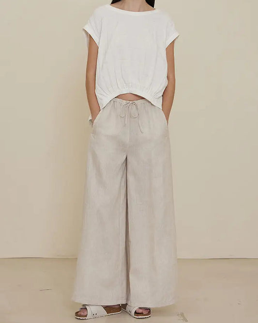 A model wearing long line linen pants with a wide fit and a white cropped top.