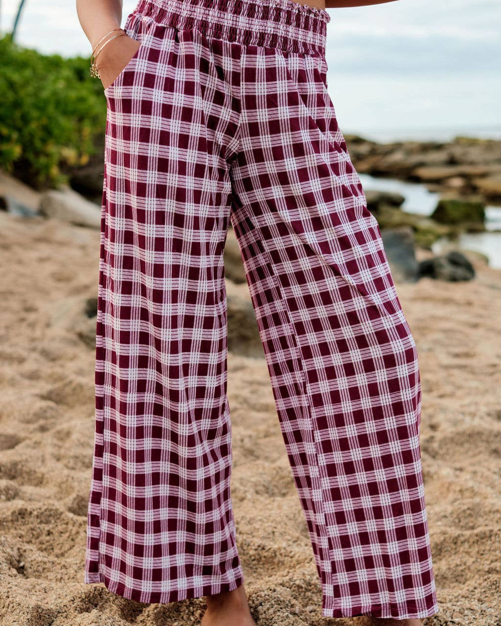A person standing on a beach wearing red and black palaka pants with a matching top