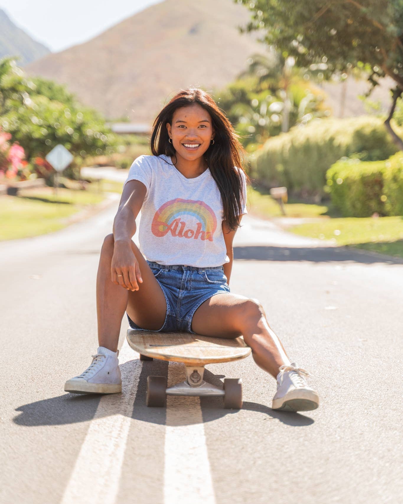 Woman sitting on a skateboard wearing a t-shirt with a rainbow design 
